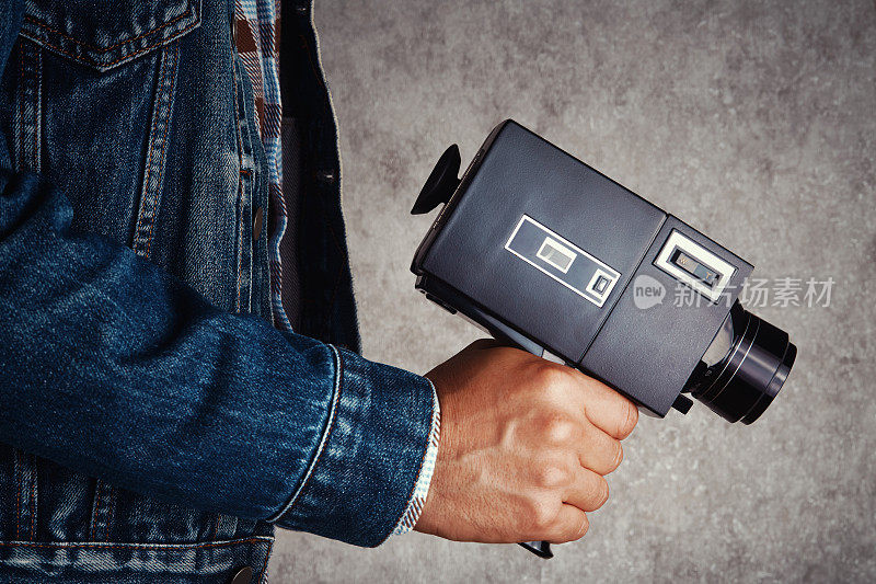 电影摄影师拿着老式模拟Super8, 8毫米电影摄影机在混凝土墙前。把相机对准枪